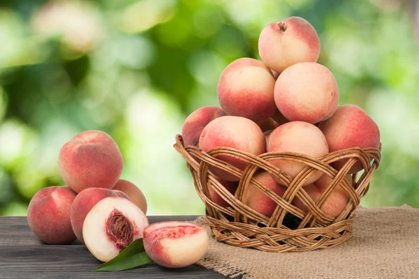 Peaches in a wicker basket on wooden table with blurred background — Stock Photo, Image