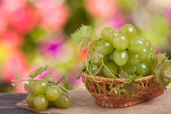 Raisins verts dans un panier en osier sur une table en bois avec fond flou — Photo