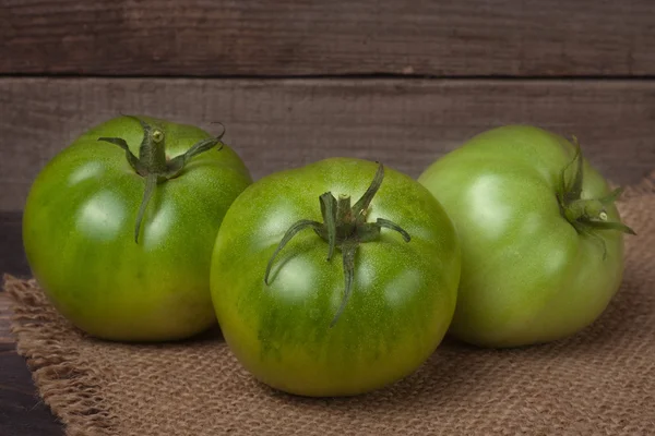 Drei grüne unreife Tomaten auf dem hölzernen Hintergrund mit Klette — Stockfoto