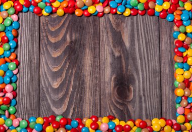 Frame of colorful candy on wood background  clipart