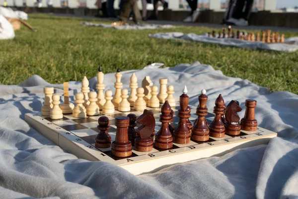 Üzerinde gri bir battaniyenin üzerinde parktaki figürler olan tahta bir satranç tahtası..