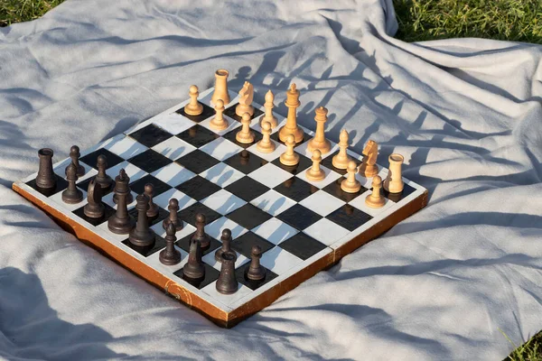Eski ahşap satranç tahtası. Parkta gri bir battaniye var..