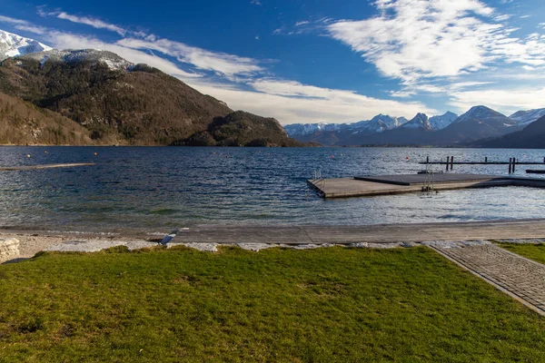 春の時間霜の風景天気の良い日に雪のピークと木製の桟橋と山の背景と湖の海岸線の景色オーストリアで3月の日の時間 — ストック写真
