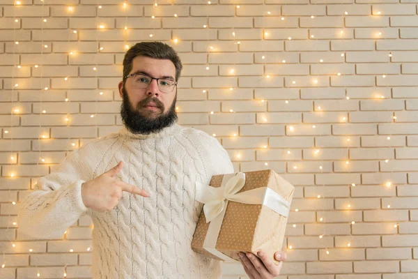 头戴圣诞礼物的大胡子男子在温暖舒适的演播室里摆姿势 房间里点缀着黄色灯笼 背景是白色砖墙 — 图库照片