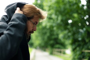 Kapüşonlu, profil fotoğraflı, arka planda odaklanmamış manzaralı tehlikeli bir adam.