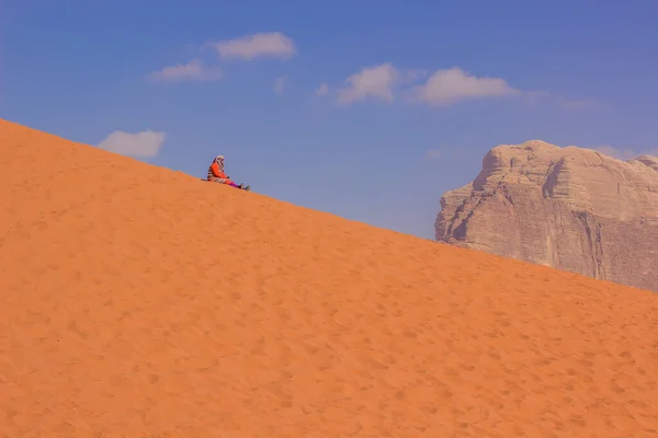 funny travel photography of old woman sit on sand of desert dune hill and rest in Wadi Rum world famous travel site of Jordan Middle East region country, yellow background in clear weather day