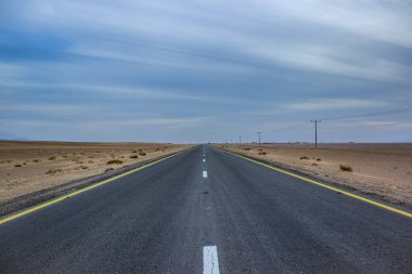 Çöl boyunca düz yol asfalt sürüş yolu boş panorama kumlu çevre manzarası ufuk minimalizm stili fotoğrafçılık bulutlu bulutlu hava saatinde