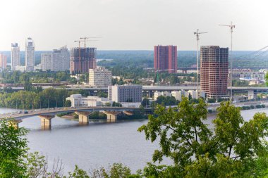 Geniş panorama şehri manzara gelişimi ülke sanayisi Ukrayna 'nın Kyiv kentindeki Dinyeper nehri üzerinde kargo ve çalışan nesneler ile tamamlanmamış yüksek binalar ve köprü ile nehir kıyısına bakıyor.