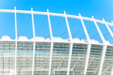 Stadyum mimarisi dış yapı geometrik desen sütunlar mavi gökyüzü arkaplan görünümünde beyaz malzeme duvarlar