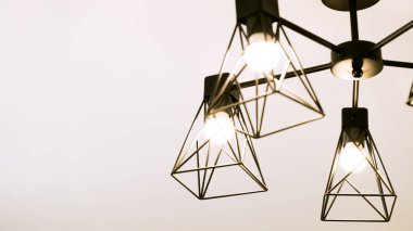 Yumuşak odadaki tavan arası avizesi nötr iç mekan arkaplan bej pastel renk panorama formatında ışık saçıyor.