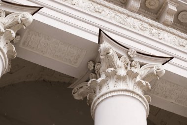 Beyaz Korint sütun başkentinin yakın görüntüsü, ayrıntılı akanthus yaprakları, voltajlar ve bir bina cephesine karşı çiçek süsleri sergiliyor.