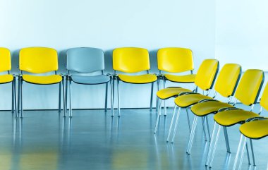 Bir sıra boş sandalye, bazıları parlak sarı ve bir gri, parlak mavi bir duvara karşı, yansıyan parlak zemin