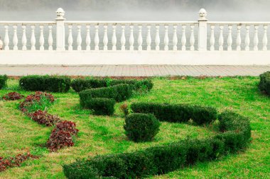 Düzgün budanmış boxwood çitleri ve süs bitkileri beyaz bir balyoz ve sisli bir su kütlesinin yanında huzurlu bir manzara yaratır.