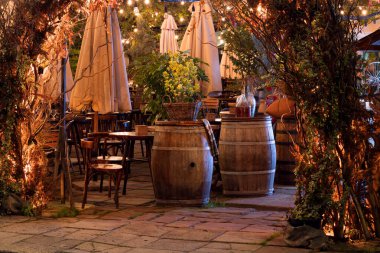 Alacakaranlıktaki boş bir avrupa tarzı teras restoranının büyüleyici atmosferi. Sıcak peri ışıklarıyla aydınlatılmış ve kırsal şarap fıçılarıyla süslenmiş.