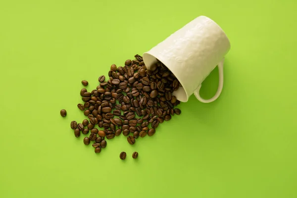 Spilled cup of roasted coffee against green background,flat lay
