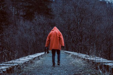 Elinde maskesi olan turuncu kapüşonlu bir adam eski terk edilmiş demiryolu viyagiyla.