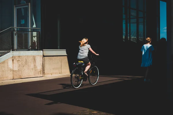 Kadın bisiklet sürüyor, kısmen gölgede, Varşova sokaklarında.