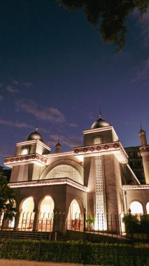Güzel aydınlatılmış bir cami alacakaranlık gökyüzünün altında duruyor. Sıcak aydınlatma ve zarif kubbelerle güçlendirilmiş karmaşık mimari ve dingin ortam sergiliyor..