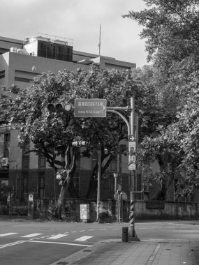 Ağaçlar ve modern binalarla çevrili bir yol tabelasının yer aldığı bir şehir caddesi, doğal gün ışığında günlük bir şehir ortamını yakalıyor..