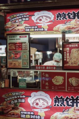 İnsanlar Gongguan Gece Pazarı 'nın yanında oturmuş modern bina ışıklarıyla aydınlanıyor ve hareketli bir gece ortamı yaratıyorlar..