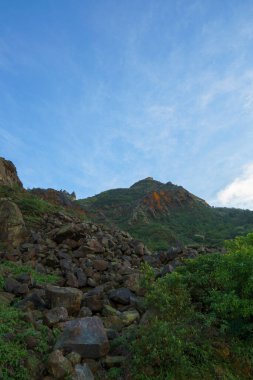 Sakin bir yol, dramatik bulutlu bir gökyüzünün altında yeşil dağ tepelerine çıkar, doğal manzarayı, açık havayı ve huzurlu atmosferi yakalar..