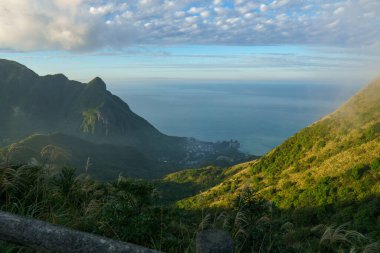 Mavi gökyüzünün altında denize doğru açılan yeşil bir dağ vadisinin geniş bir manzarası. Huzurlu doğa, manzara derinliği ve açık hava seyahati manzarasını yakalıyor..