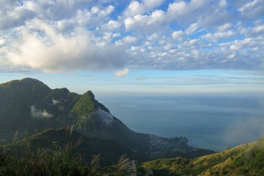 Mavi gökyüzünün altında denize doğru açılan yeşil bir dağ vadisinin geniş bir manzarası. Huzurlu doğa, manzara derinliği ve açık hava seyahati manzarasını yakalıyor..