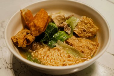 Tofu, sebze ve lezzetli et suyuyla servis edilen sıcak şehriye çorbası. Sıcak ışıklandırmalı konforlu yiyecek konsepti, Asya mutfağına uygun, ev yapımı yemekler, ve gündelik yemek temaları.