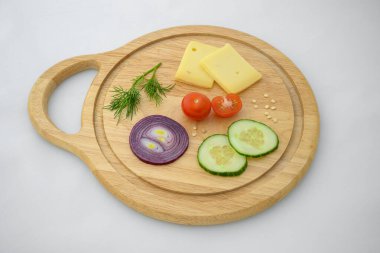 Peynir ve sebzeler doğrama tahtasında. Soğan, salatalık ve kiraz domatesleri..