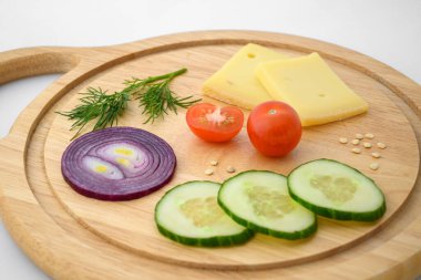 Peynir ve sebzeler doğrama tahtasında. Soğan, salatalık ve kiraz domatesleri..