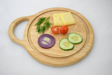Peynir ve sebzeler doğrama tahtasında. Soğan, salatalık ve kiraz domatesleri..