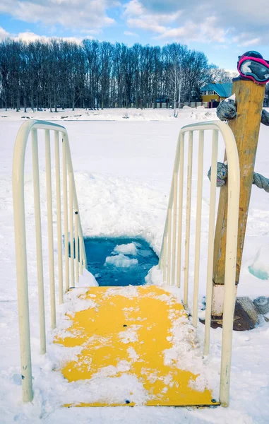 The ice-hole for winter swimming in harsh conditions. The yellow staircase with railing leading to ice cold water.