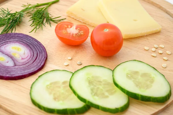 Peynir ve sebzeler doğrama tahtasında. Soğan, salatalık ve kiraz domatesleri..