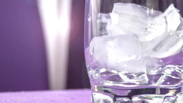 Таяние кубиков льда в стекле. Размытый фиолетовый фон с закатом. — стоковое видео