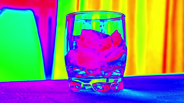 Bardakta renkli eriyen buz küpleri. Arkaplanda gökkuşağı gibi görünen bir masa ve şeffaf cam.. — Stok video