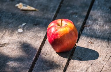 Güneş tarafından aydınlatılan kırmızı elma eski ahşap bir yüzeye gölge düşürür. Durgun yaşam, sağlıklı yaşam, beslenme, diyet, açık hava, hasat, rastgele çerçeve.