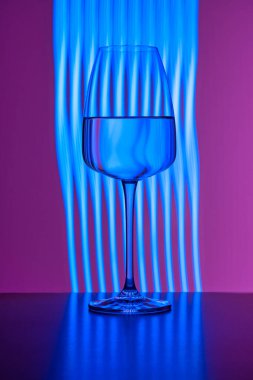 Mor zemin üzerinde mavi ışıkla boyanmış saf suyla dolu kristal cam. Sıçrama yok, yüzeyde bile. Hayat, restoran bardakları, servis, romantizm, tutku, içecek..