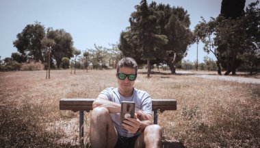 Parkta cep telefonuna bakıp egzersiz yapan bir adam.