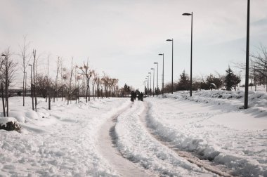 Issız bir caddede karda yürüyen bir grup uzlaşılmaz insan.