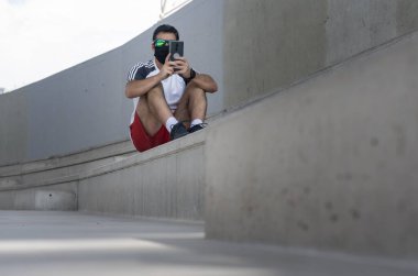 Spor kıyafetli bir adam tribünün merdivenlerinde akıllı telefonuna bakıyor.