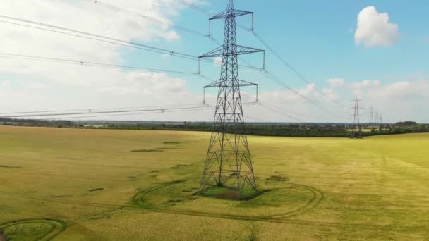 Imágenes de drones repasando un pilón de electricidad sobre campos amarillos con cielo azul — Vídeos de Stock