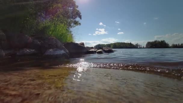 Pequenas ondas na margem do lago rochosa. Luz solar a brilhar na água. Belo dia de verão — Vídeo de Stock