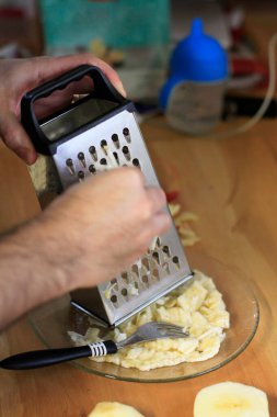 Elleri tabakta kırmızı bir elma rendeliyor.