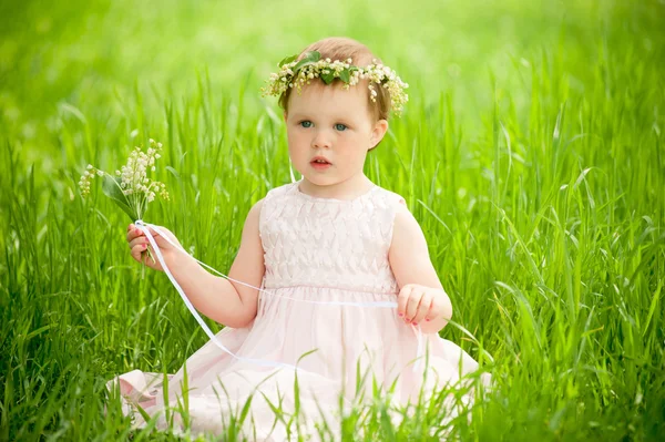 Γλυκό κοριτσάκι στο στεφάνι από λουλούδια που κάθεται στο πράσινο γρασίδι σε εξωτερικούς χώρους — Φωτογραφία Αρχείου