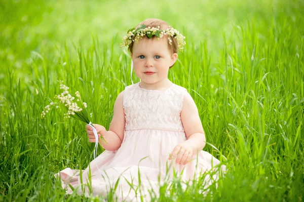 Doux bébé fille en couronne de fleurs assis sur l'herbe verte à l'extérieur — Photo
