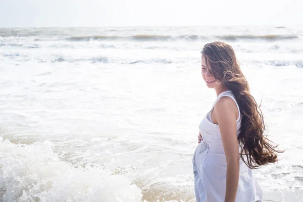 Красивая беременная женщина, улыбающаяся на берегу моря — стоковое фото