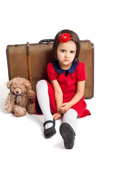 Menina bonita infeliz no vestido vermelho com mala e urso de brinquedo — Fotografia de Stock