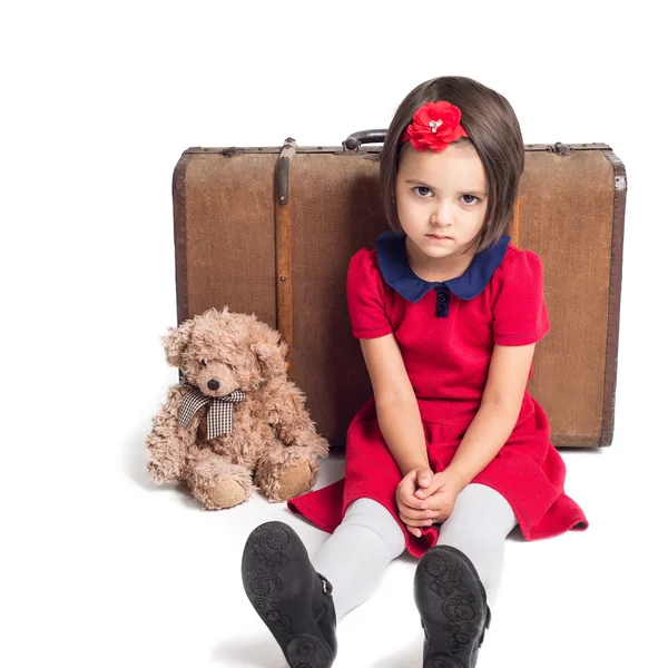 Menina bonita infeliz no vestido vermelho com mala e urso de brinquedo — Fotografia de Stock