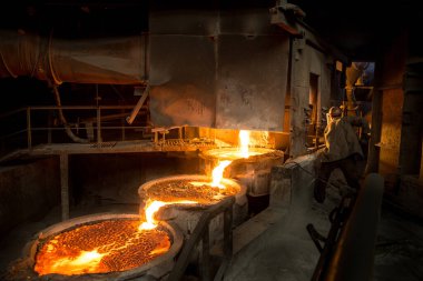 Ark fırınının yanında çelik işçisi çalışıyor ve sıvı metal dökülüyor.