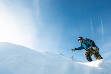 Karlı dağlarda buz baltasıyla yürüyen bir dağcı.